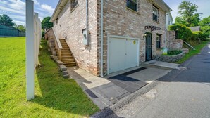 A two-story brick building with a white garage door, a small front porch, and a set of stairs leading to the entrance. - 4 Mi to Off-road Park: Beckley Area Townhome (Sophia)