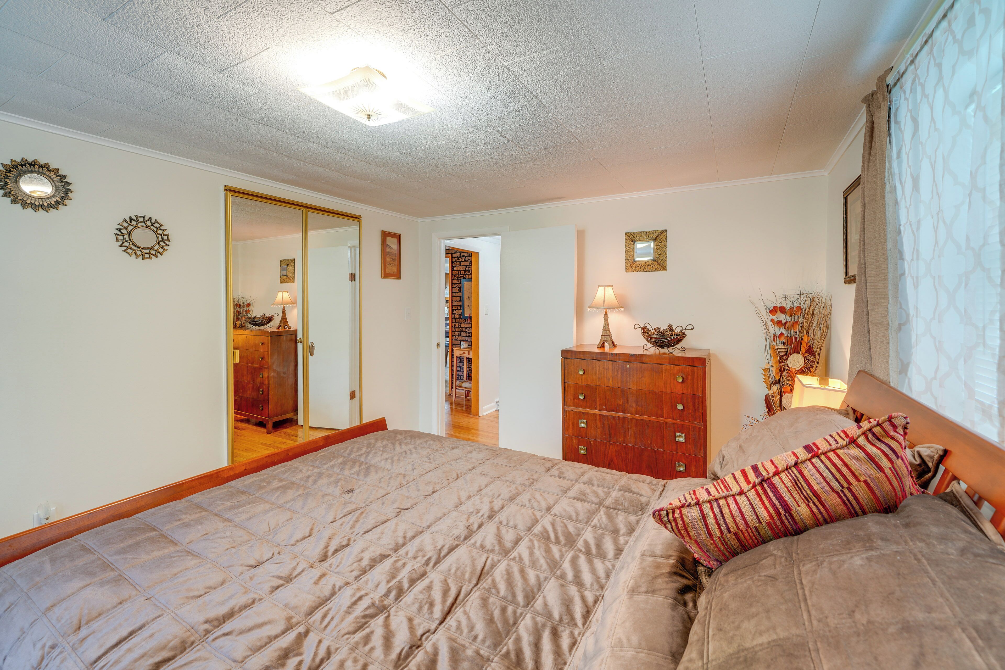 A bedroom with a large bed, a dresser, a mirror, and a door leading to another room.