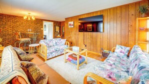 A cozy living room with a brick wall, wooden paneling, a sofa set, a coffee table, and a small dining area. - 4 Mi to Off-road Park: Beckley Area Townhome (Sophia)