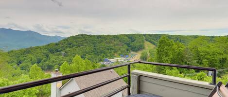 A balcony with a table and chairs overlooking a forested mountain area.