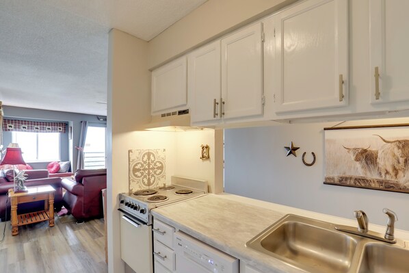 A compact kitchen with white cabinets, a stove, and a sink. There is a dining area with a table and chairs, and a living room with a sofa and a lamp. - Indoor & Outdoor Pools! Condo 3 Mi to Gsmnp (Gatlinburg)