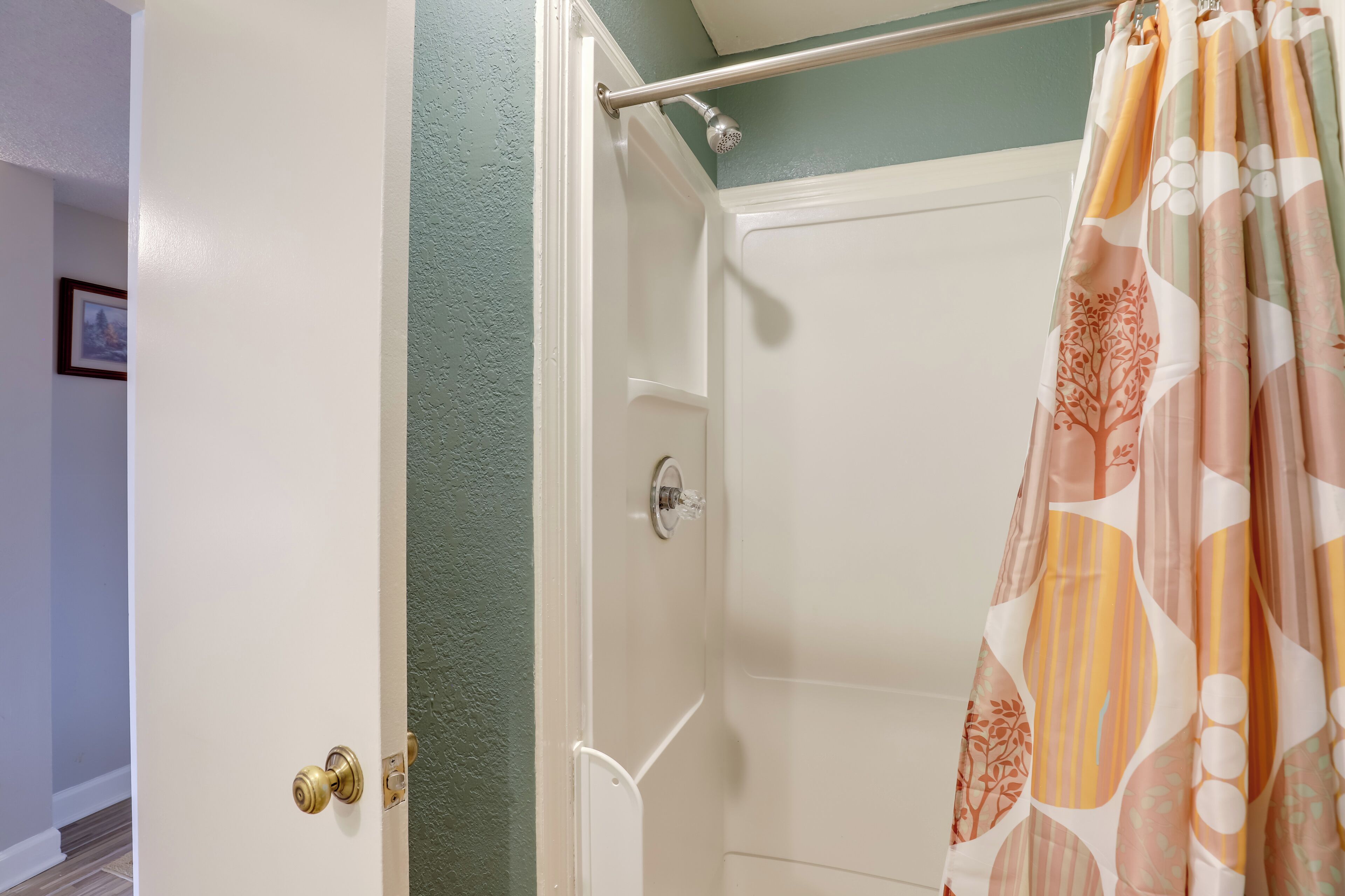 A bathroom with a shower curtain, a door with a brass doorknob, and a green wall.