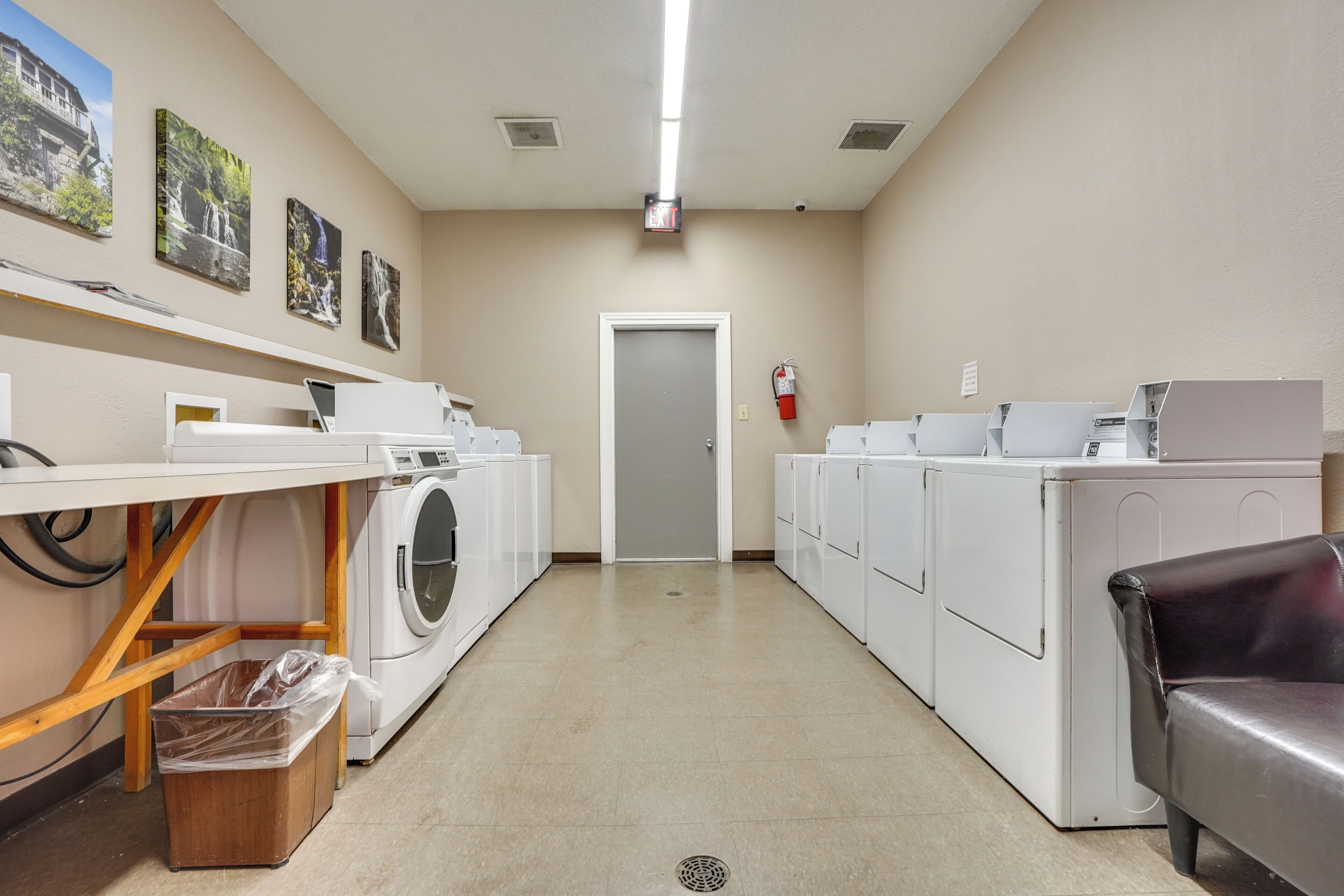 A laundry room with multiple washing machines, a fire extinguisher, and a door at the end.