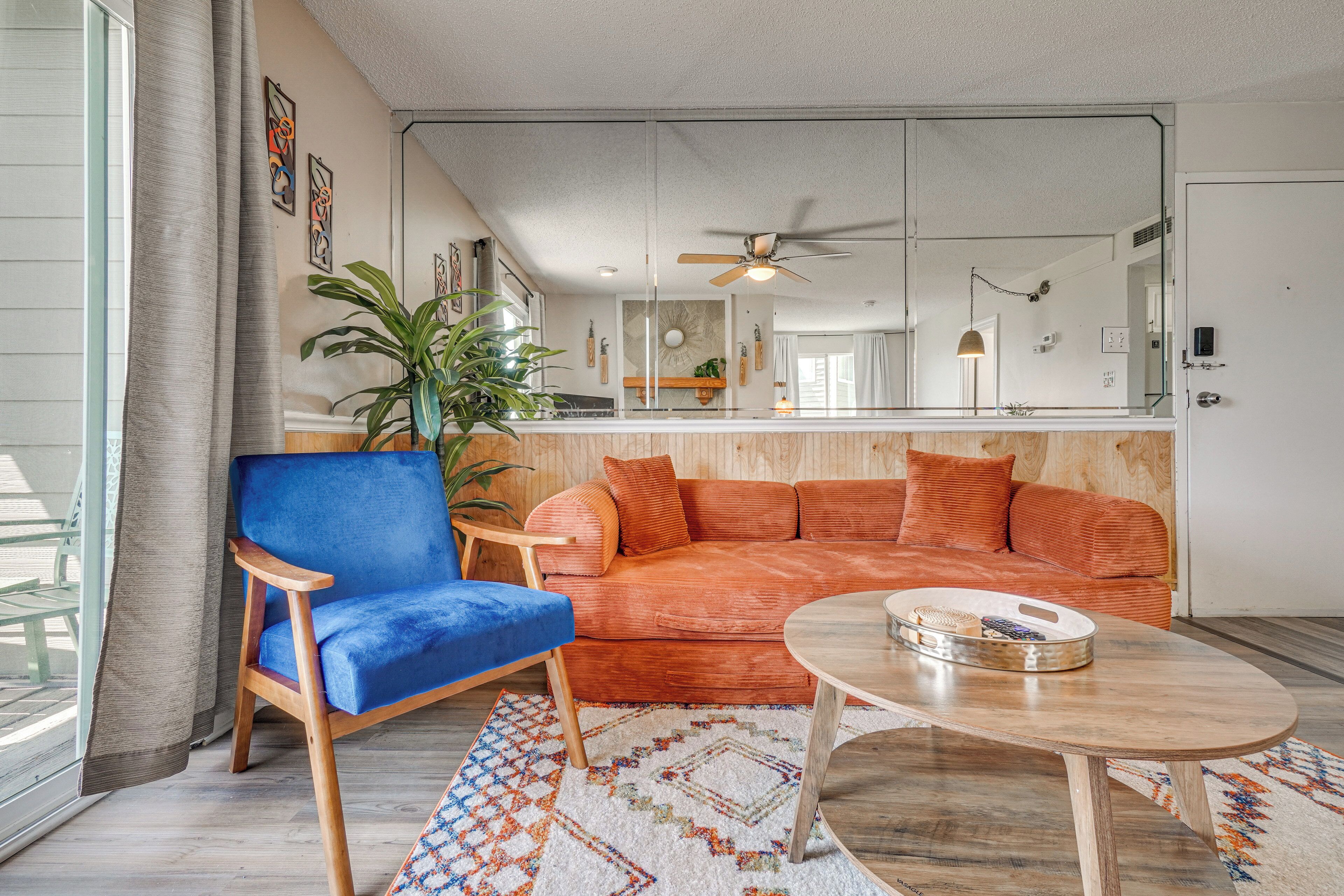 Una sala de estar con una butaca azul, un sofá naranja, una mesa de centro de madera y un tapete estampado.