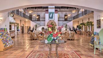 A spacious lobby with a central round table, multiple seating areas, and a staircase leading to an upper level.