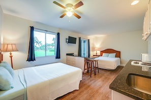 A hotel room with two beds, a kitchenette, a ceiling fan, and a TV.