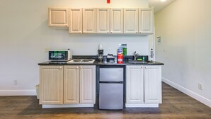Une cuisine avec des meubles de rangement en bois clair, un réfrigérateur en acier inoxydable, un four à micro-ondes et une machine à café.