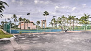 A sports court with a fence, palm trees, and a building with a clock tower.