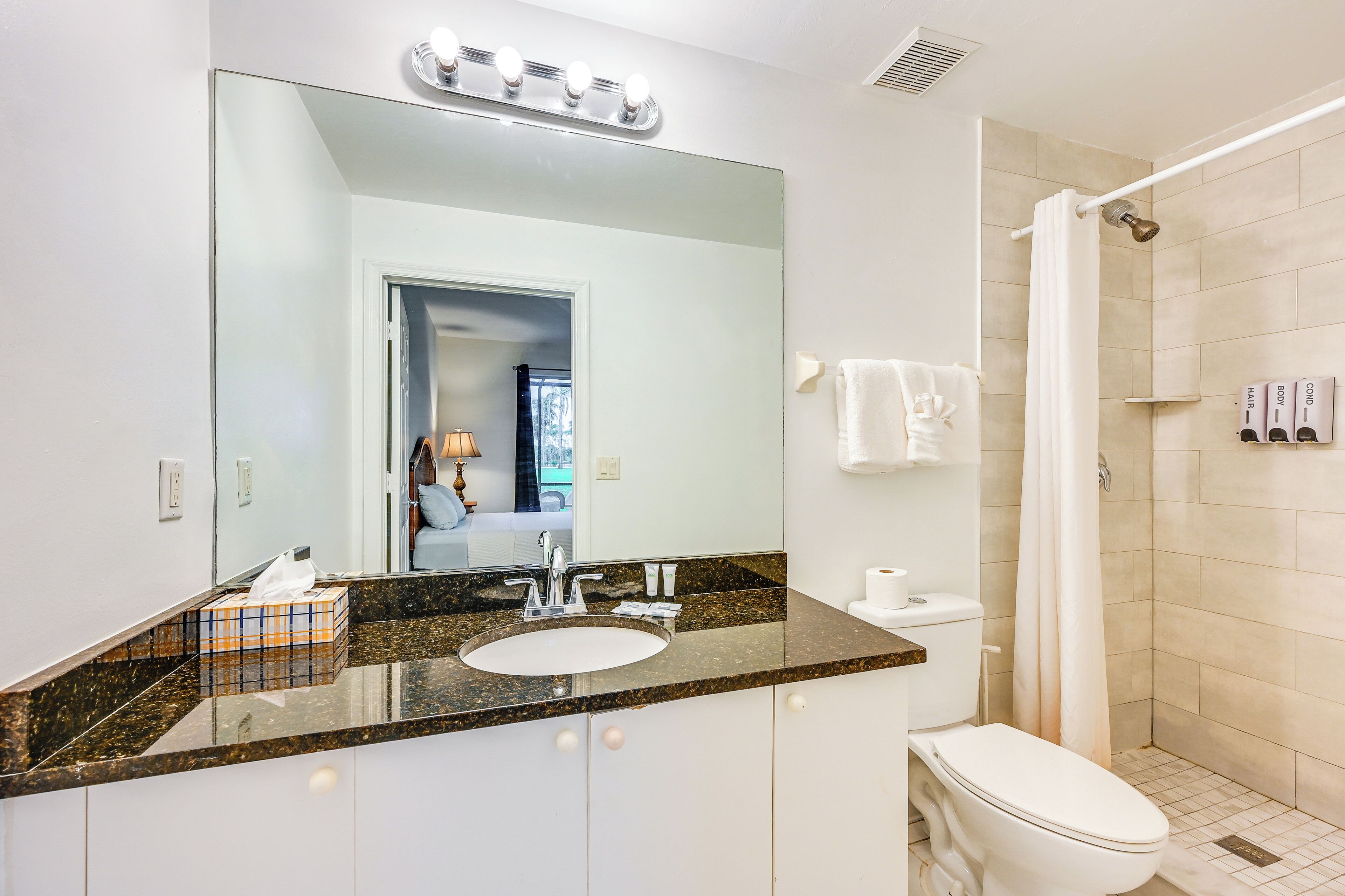 Une salle de bain comprenant un grand miroir, un lavabo, des toilettes et un espace douche.