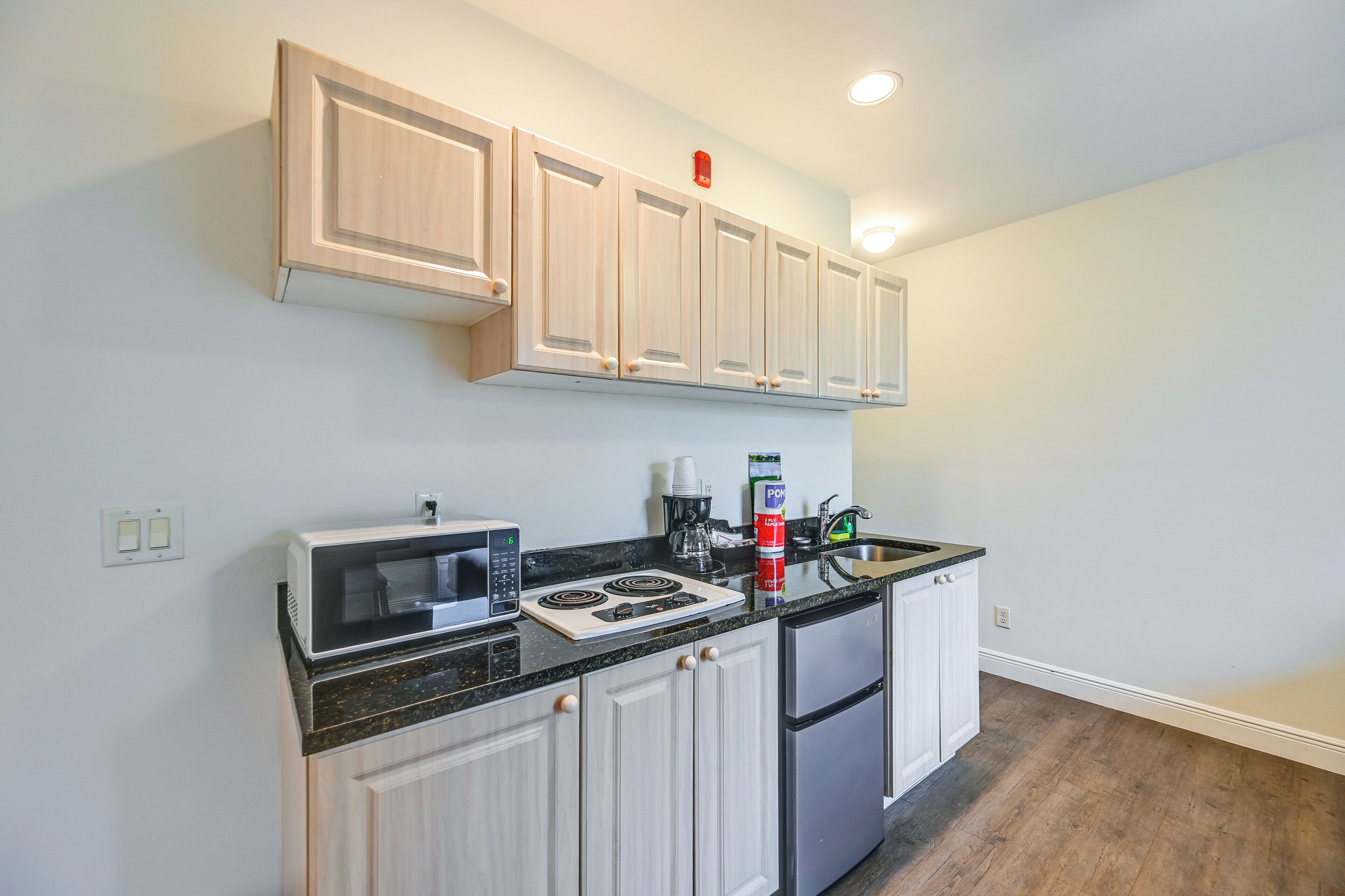 A modern kitchen with light wood cabinets, a black countertop, a built-in microwave, a stove, and a refrigerator.