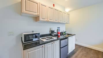 A modern kitchen with light wood cabinets, a black countertop, a built-in microwave, a stove, and a refrigerator.