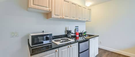 A modern kitchen with light wood cabinets, a black countertop, a built-in microwave, a stove, and a refrigerator.