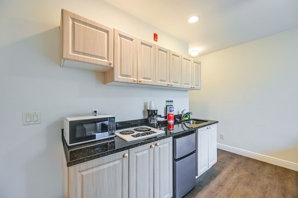 A modern kitchen with light wood cabinets, a black countertop, a built-in microwave, a stove, and a refrigerator.