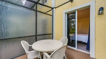 A covered patio with a table and chairs, a sliding glass door leading to a bedroom, and a small outdoor light fixture.
