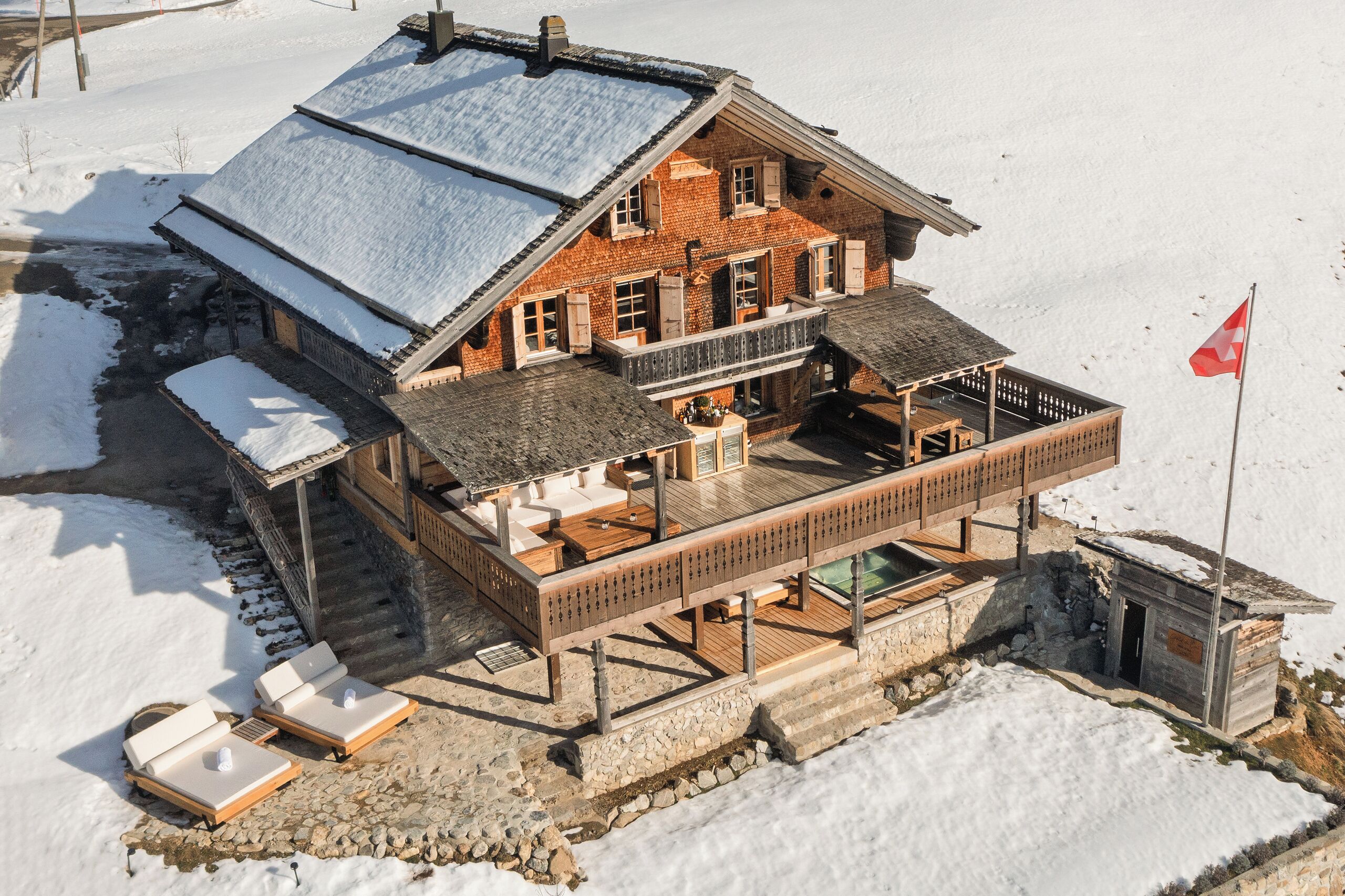 A chalet with a wooden deck, outdoor seating, and a flag.