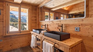 Baño de cabaña de madera con dos lavamanos, un espejo grande y una ventana con vista a las montañas.