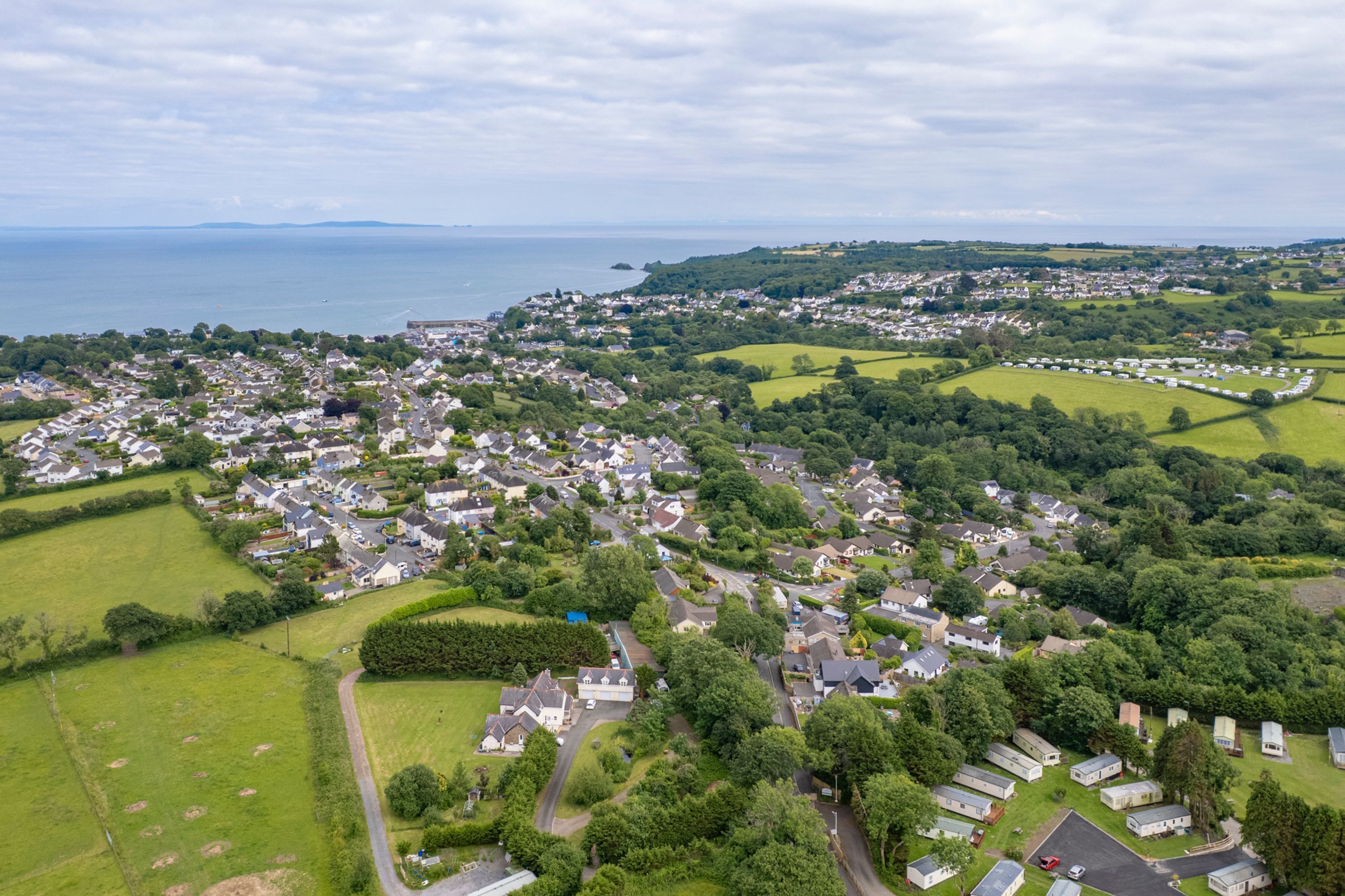 An aerial view of a residential area with houses, green spaces, and a body of water in the background.