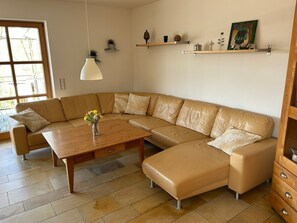 A modern living room with a leather sectional sofa, a wooden coffee table, and a vase of flowers. There are shelves with decorative items and a painting on the wall.