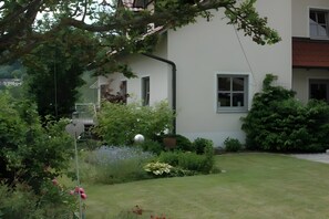 A residential building with a white exterior, a visible window, and a garden with various plants and a heart-shaped sign.