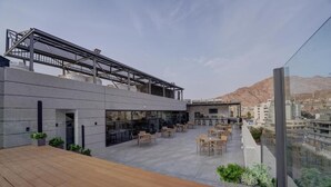 A rooftop terrace with outdoor seating, a pergola, and a view of the city and mountains.