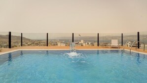 A rooftop pool with a clear view of a cityscape and mountains in the background.