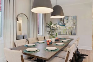 Een eetkamer met een lange tafel gedekt voor zes personen, omringd door stoelen, met een grote spiegel aan de muur en een schilderij boven de tafel.