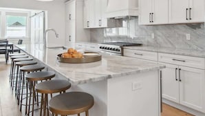 Een moderne keuken met witte kasten, een marmeren aanrecht en een centraal kookeiland met barstoelen.