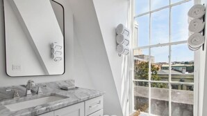 Een moderne badkamer met een grote spiegel, een marmeren aanrechtblad en een uitzicht op de stad door een groot raam.