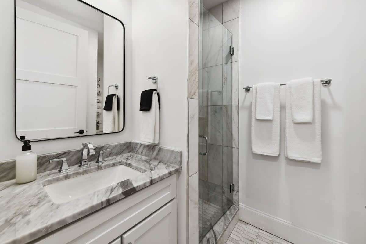 A modern bathroom with a marble sink, a large mirror, and a glass-enclosed shower.