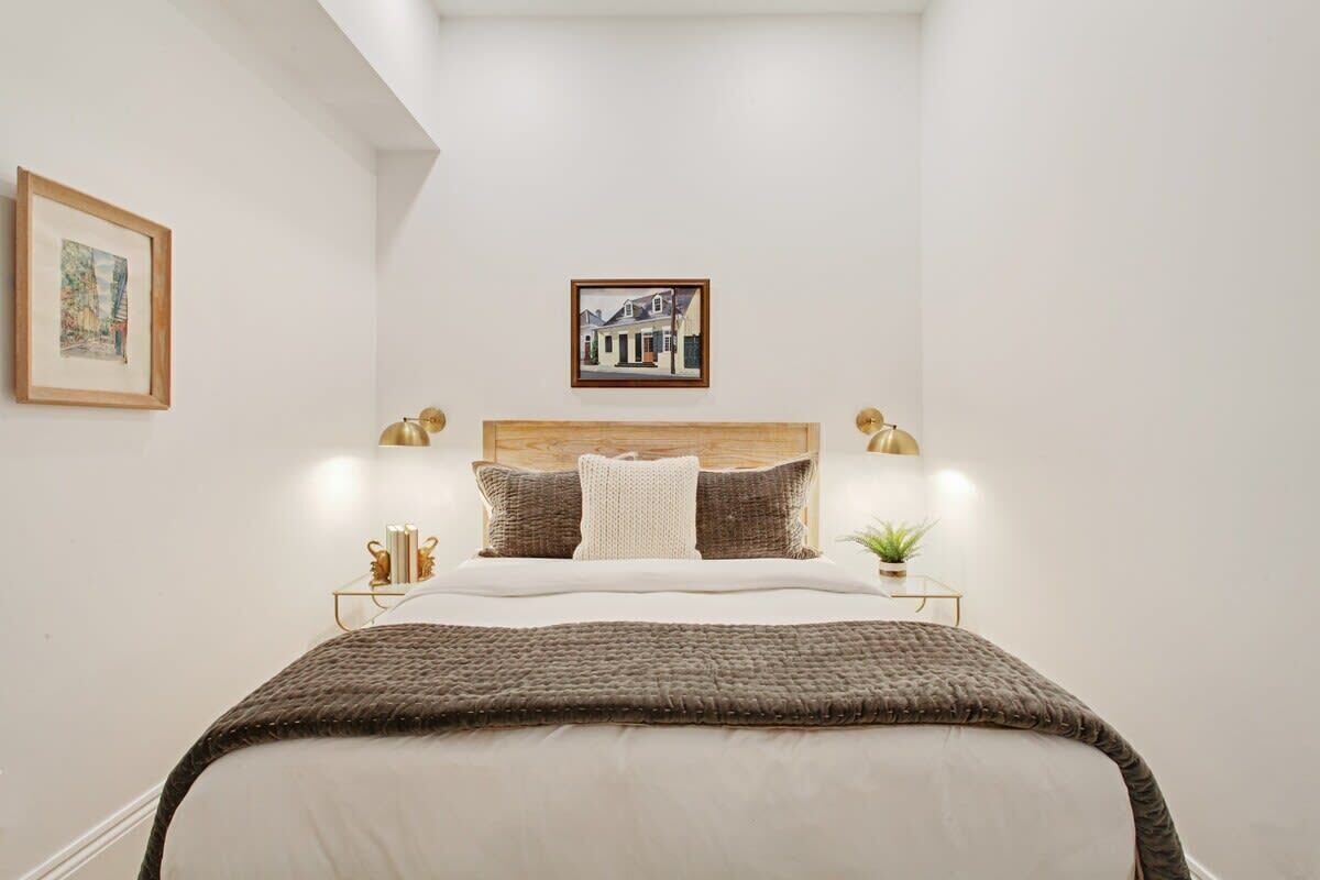 Una camera da letto ordinata con un letto grande, una testiera in legno, due lampade da comodino, un quadro appeso e una piccola pianta sul tavolino.