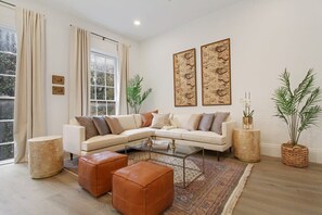En moderne stue med en hjørnesofa, et sofabord i glas og dekorative planter.