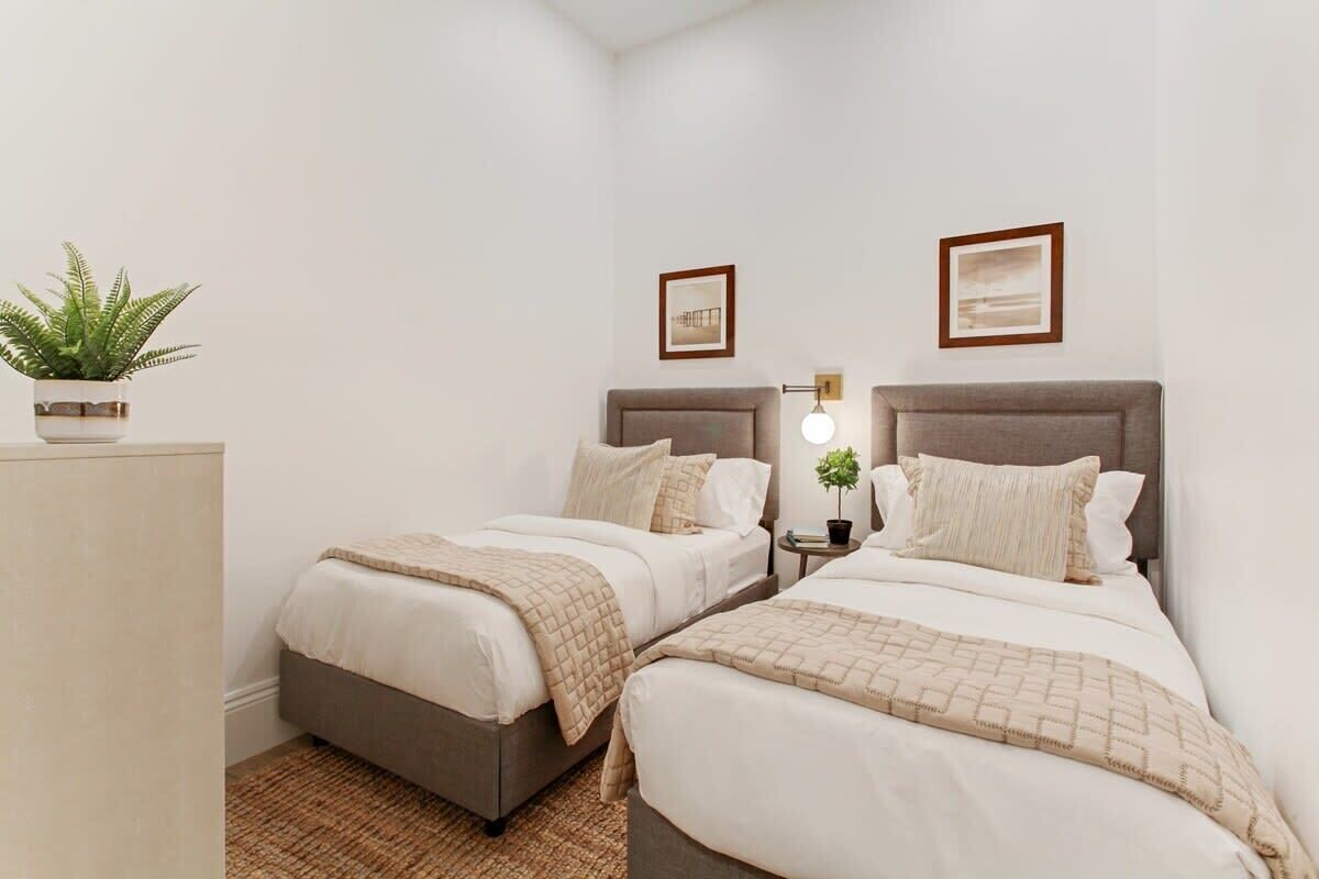 A hotel room with two beds, a nightstand with a lamp, and a potted plant.