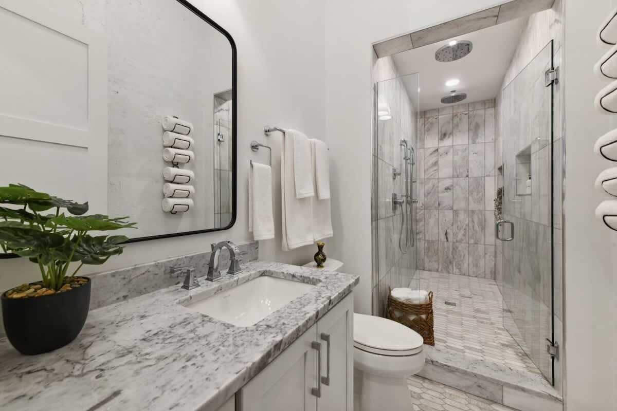 A modern bathroom with a marble sink, a glass shower enclosure, and a potted plant.