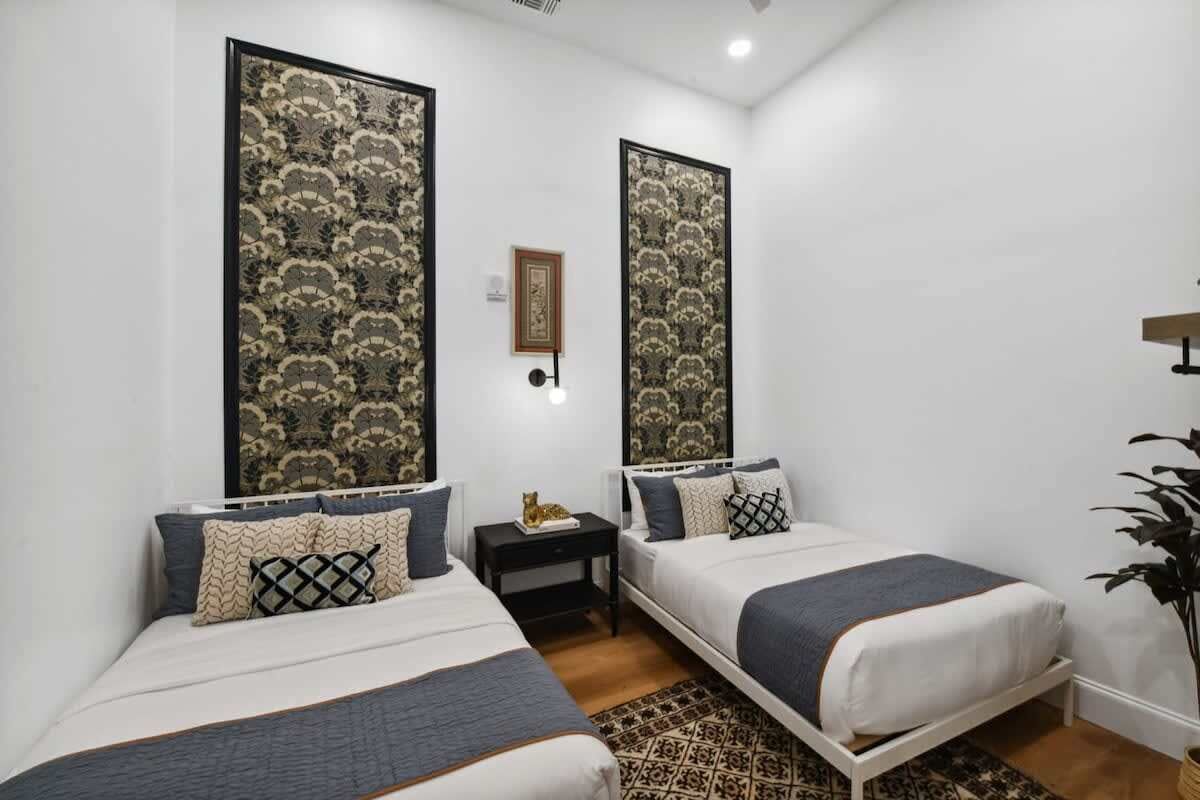 A bedroom with two beds, a nightstand, a framed picture, and a plant.