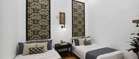 A bedroom with two beds, a nightstand, a framed picture, and a plant.