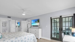 A bedroom with a bed, a television, a ceiling fan, and a sliding glass door to the outside.