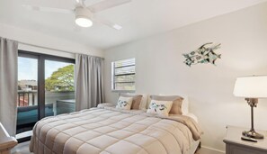 Ein Schlafzimmer mit einem großen Bett, einem Deckenventilator, einem Fenster mit Jalousien und einer Wandlampe.