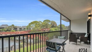 A balcony with a table and chairs, a view of a bridge, and a body of water.