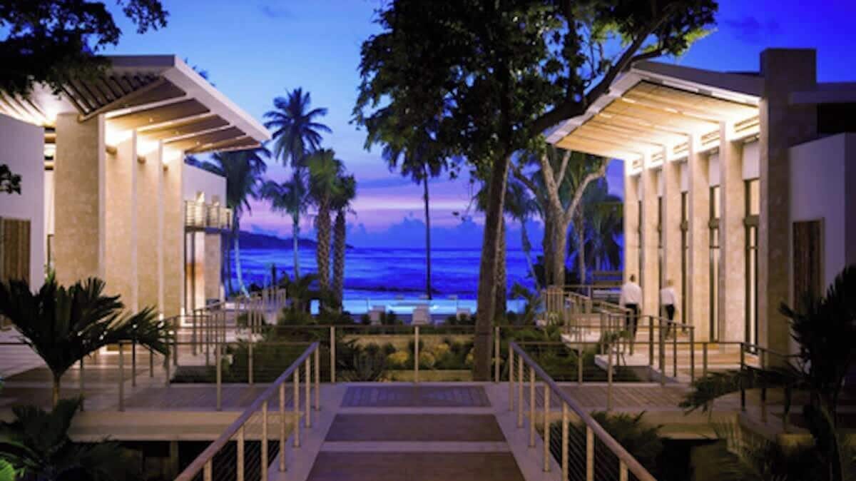 A resort with a pool, palm trees, and a view of the ocean at dusk.