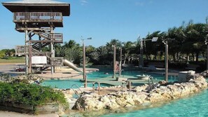 A pool area with a wooden observation tower, lounge chairs, and a clear blue pool surrounded by rocks and palm trees.