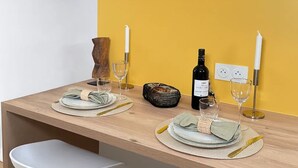 Une table à manger dressée avec des assiettes, des verres, une bouteille et des bougies, le tout placé devant un mur jaune.