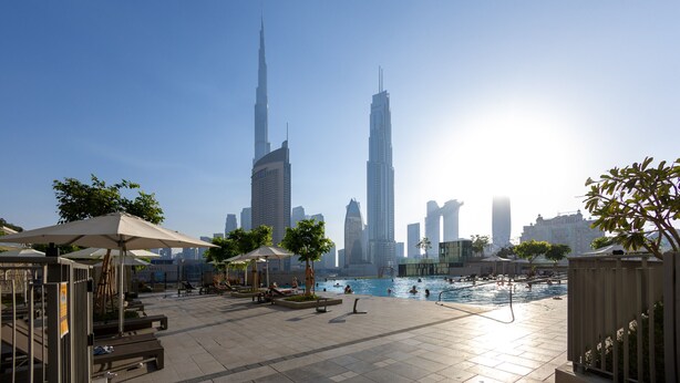 A pool area with lounge chairs and umbrellas, surrounded by tall buildings, including a prominent skyscraper.