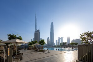 A pool area with lounge chairs and umbrellas, surrounded by tall buildings, including a prominent skyscraper.