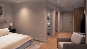 Un dormitorio moderno con cama, mesita de noche, lámpara y una silla. Se ve un pasillo que conduce a un armario y una puerta.