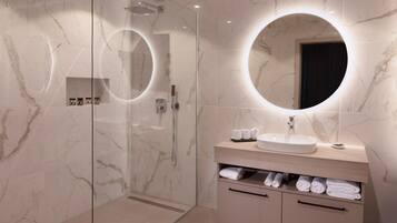 Een moderne badkamer met een douchecabine van glas, een ronde spiegel en een wastafelmeubel met een wastafel en opbergruimte voor handdoeken.