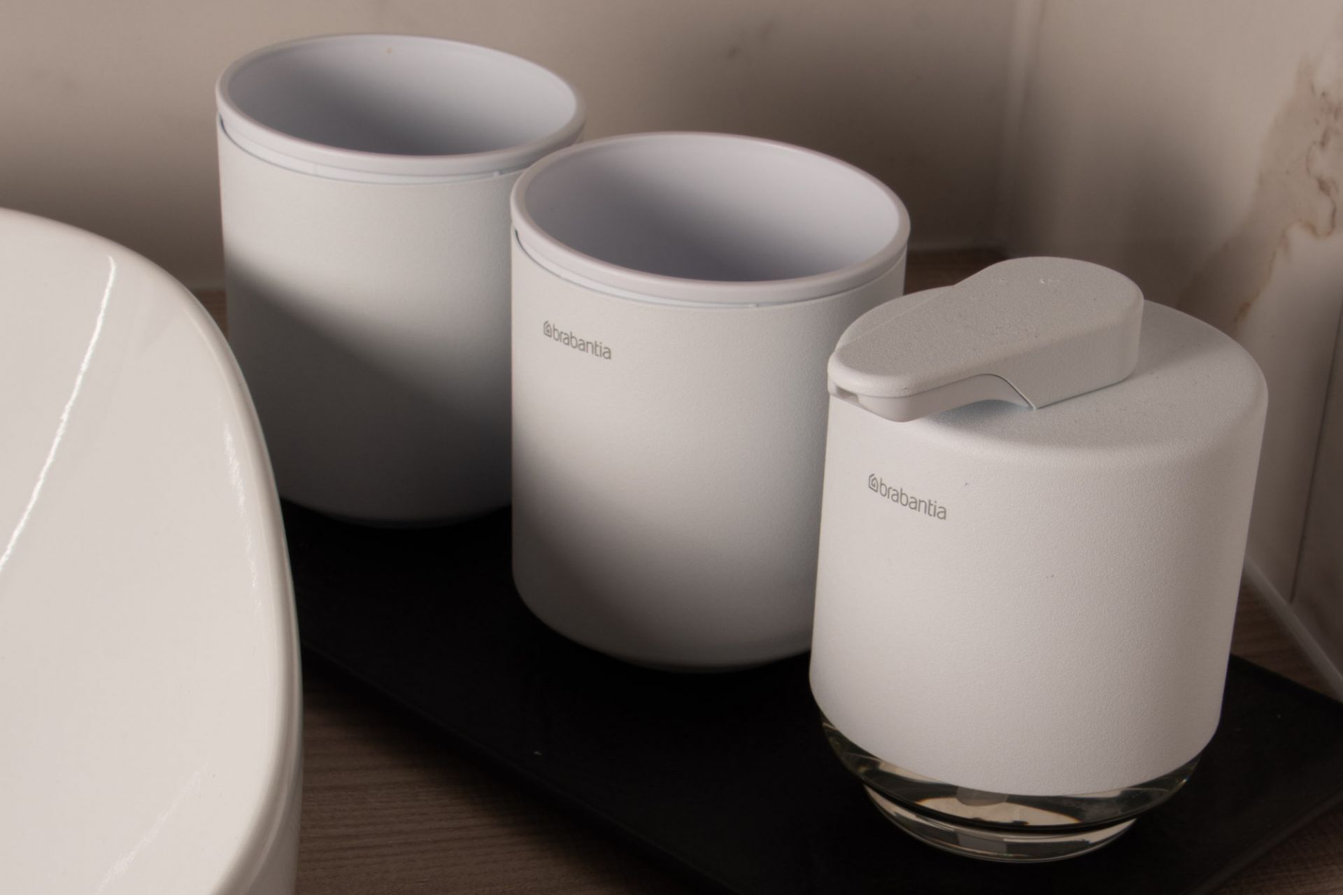 Three white cylindrical containers with handles on a black tray, placed on a wooden surface.