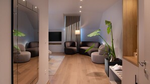 Una habitación de hotel moderna con un espejo grande, dos sofás, un televisor y una planta en maceta.