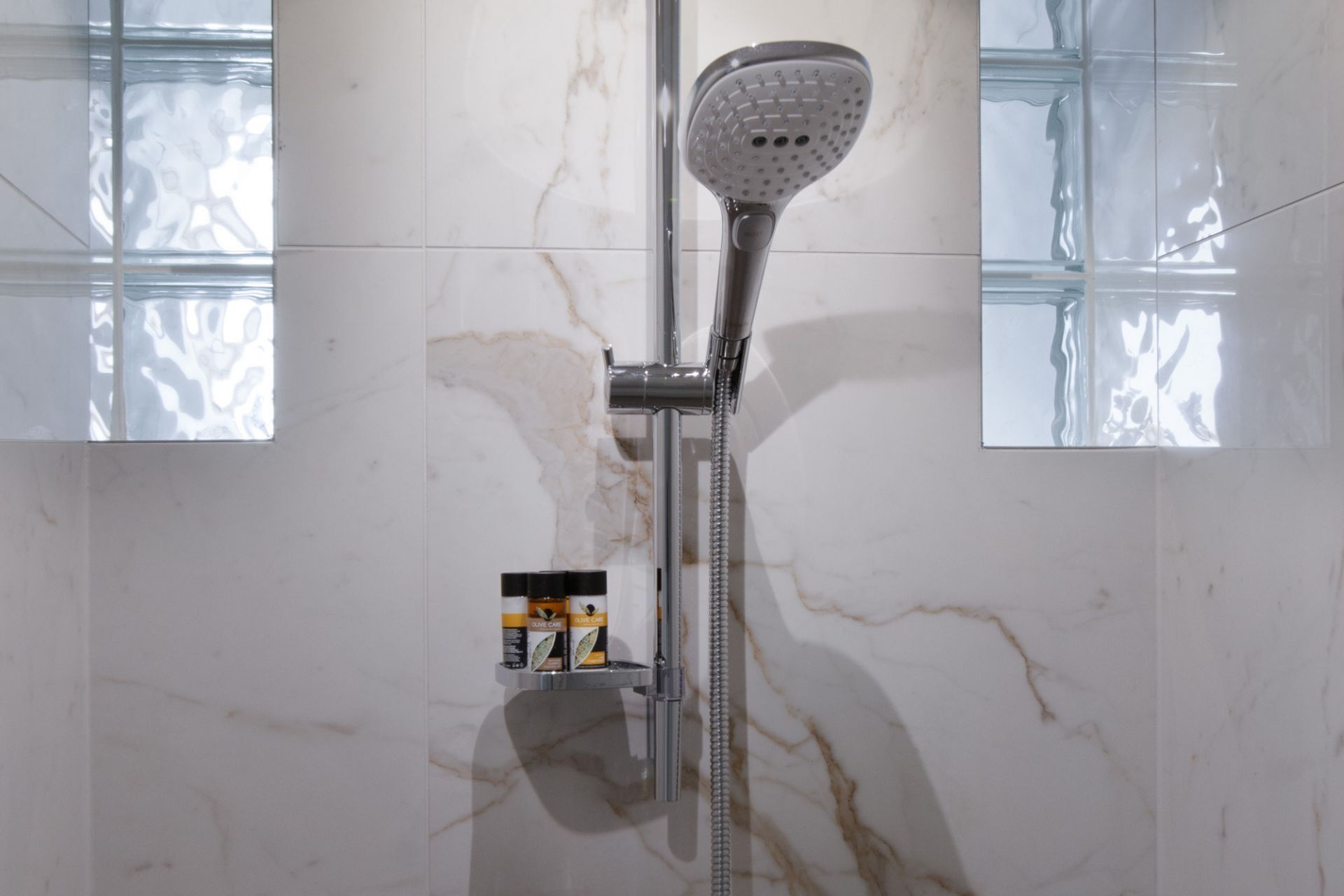 A shower with a handheld showerhead, a handheld shower attachment, and a soap dispenser on a wall-mounted shelf.