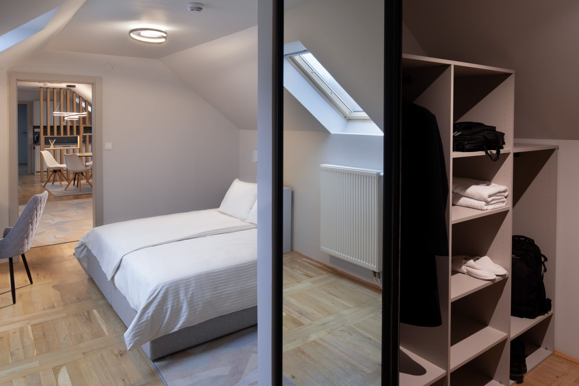 A bedroom with a bed, a wardrobe, a skylight, and a view of a dining area.