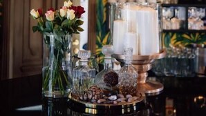 Una zona de bar con papel tapiz tropical, una variedad de botellas y un centro de mesa con velas.